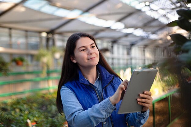 Foto vrouw die in een kas werkt en planten controleert met een tablet