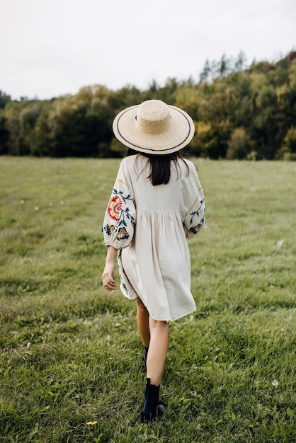 Foto vrouw die in een open veld loopt met een strohoed en een vintage bloem geborduurde jurk