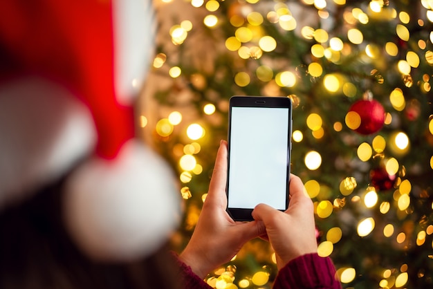 Foto vrouw die in kerstmishoed mobiele foto van mooie spar maakt