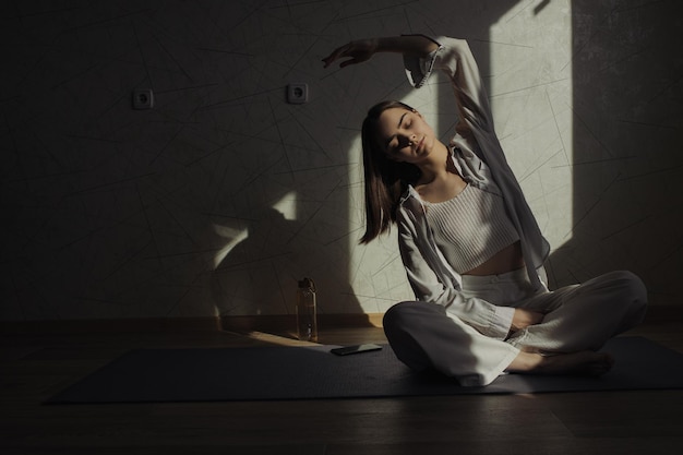 vrouw die in Lotus pose zit en buigoefeningen doet terwijl ze yoga beoefent in een zonovergoten kamer thuis