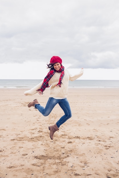 Vrouw die in modieuze warme kleding bij strand springt