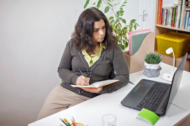 Vrouw die in notitieboekje schrijft en laptop computer bekijkt. Online onderwijs