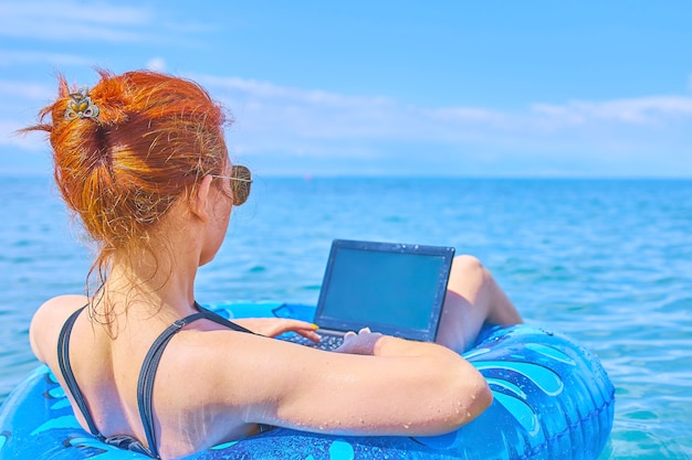 Vrouw die in opblaasbare ring op zee situeert en in laptop werkt.