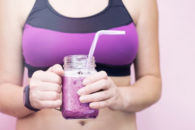 Vrouw die in sportenkleren fruitbosbessen detox smoothie na fitness training houden