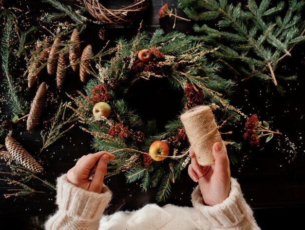 Vrouw die in witte sweater een kroon van Kerstmis maakt