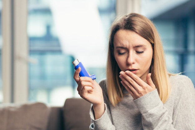 vrouw die inhalator gebruikt terwijl ze thuis aan astma lijdt