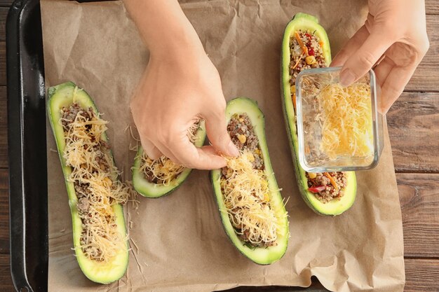 Foto vrouw die kaas toevoegt aan quinoa gevulde courgettes in de keuken