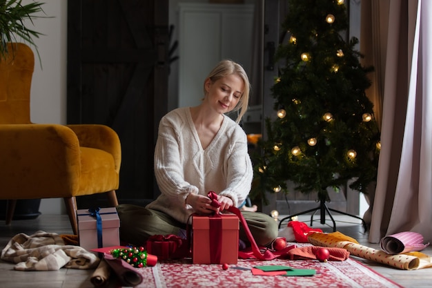 Vrouw die kerstcadeaus thuis op een vloer inpakt.