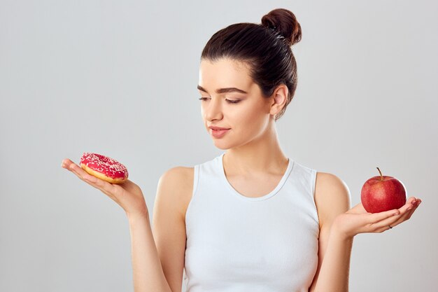 Vrouw die keuze maakt tussen appel en dessert. Dieet concept. Het donkerbruine meisje houdt een roze dessert en een appel.