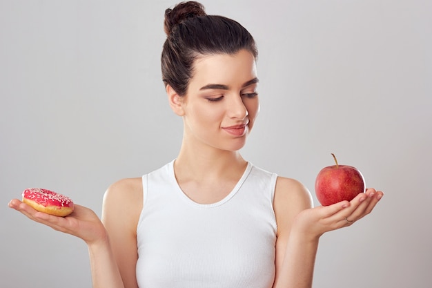 Vrouw die keuze maakt tussen appel en donut op witte achtergrond