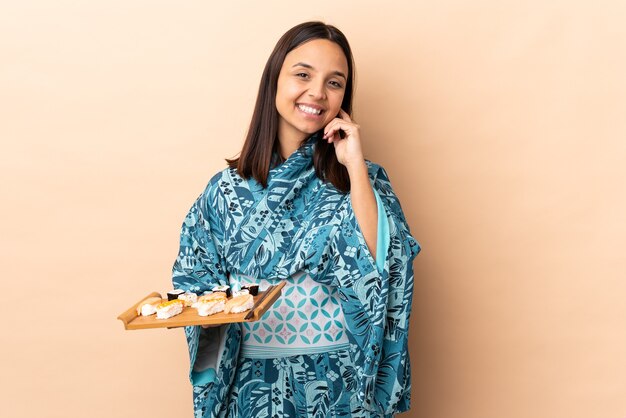 Vrouw die kimono draagt en sushi houdt over geïsoleerde muur het lachen