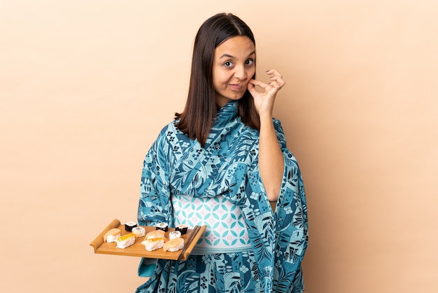 Vrouw die kimono draagt en sushi over geïsoleerde muur houdt die een teken van stiltegebaar toont