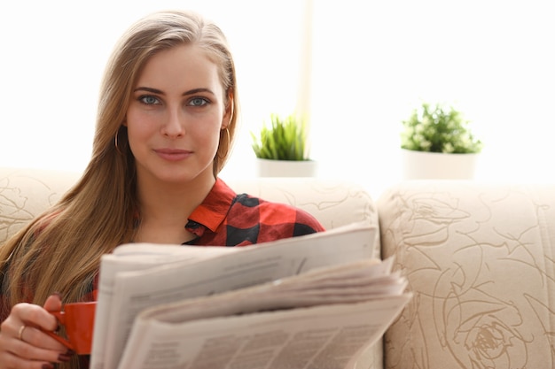 Vrouw die koffie drinkt en leest, zit op de bank