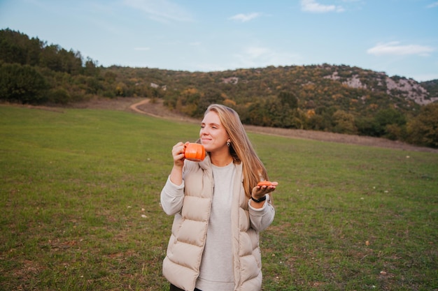 Vrouw die koffie drinkt in de campingstoel in het bos Wandelconcept