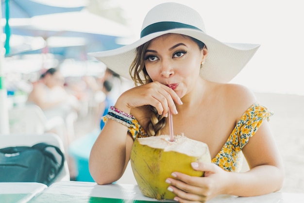 Vrouw die kokoswater drinkt. Vrouw met strandhoed die kokoswater drinkt met een rietje.