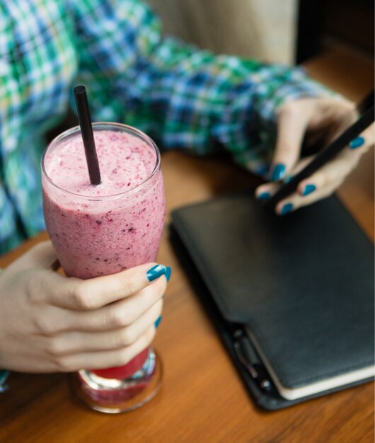 Vrouw die koude aardbeimilkshake houdt en smartphone gebruikt