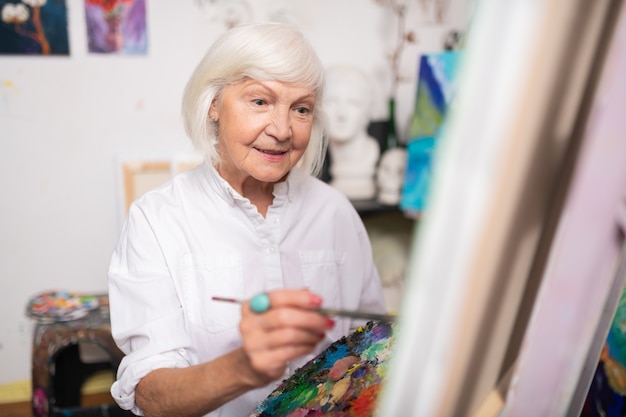 Vrouw die lacht. Aantrekkelijke oude vrouw lachend terwijl schilderij penseel en schilderen op canvas