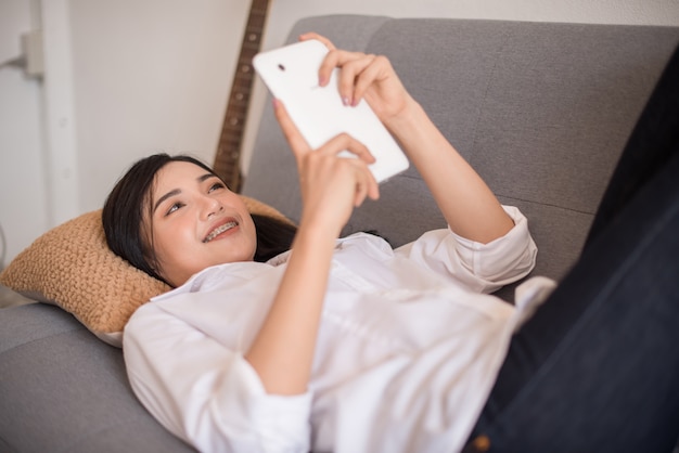 Vrouw die lacht als ze een sms-bericht op haar mobiel leest terwijl u ontspant op een bank in haar woonkamer.