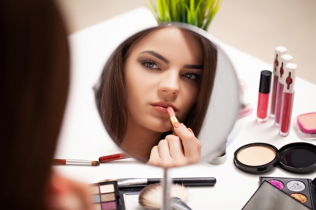 Vrouw die make-up thuis voor spiegel doet