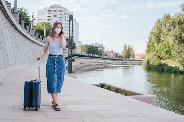 Vrouw die masker draagt en met haar koffer door de stad loopt