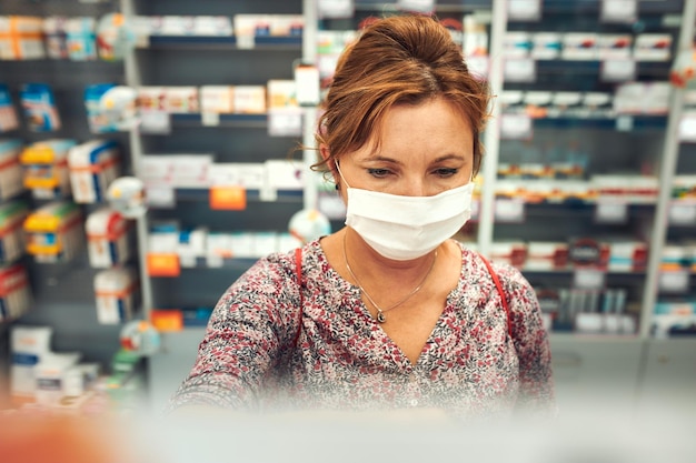 Vrouw die medicijnen koopt in een apotheek en een gezichtsmasker draagt om mond en neus te bedekken
