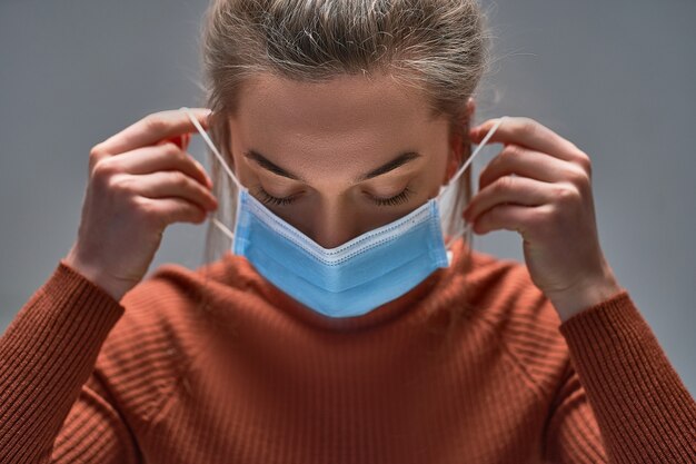 Vrouw die medisch beschermend masker opdoet voor bescherming van de gezondheid en preventie van griepvirus, epidemische en infectieziekten.