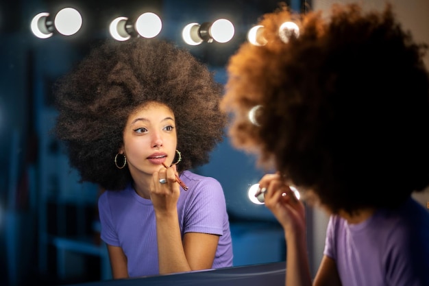 Vrouw die met Afro-kapsel make-up toepast tegen spiegel