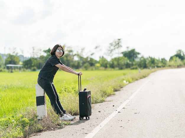 Vrouw die met bagage langs een weg liften