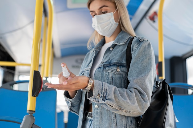 Vrouw die met de openbare bus reist en handdesinfecterend middel gebruikt terwijl ze een medisch masker draagt voor bescherming