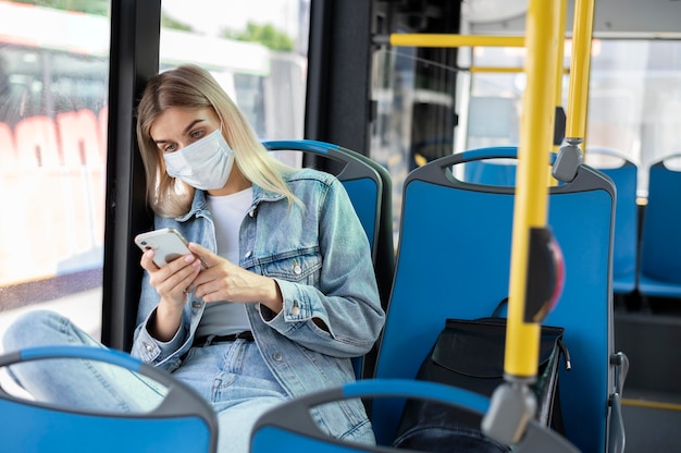 Foto vrouw die met de openbare bus reist en smartphone gebruikt terwijl ze een medisch masker draagt voor bescherming