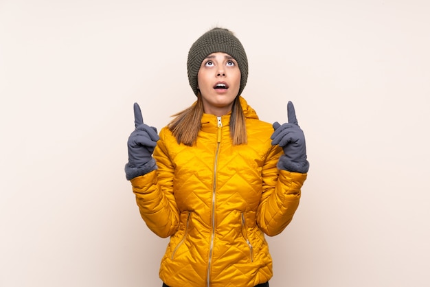 Vrouw die met de winterhoed over geïsoleerde muur met de wijsvinger een geweldig idee richt