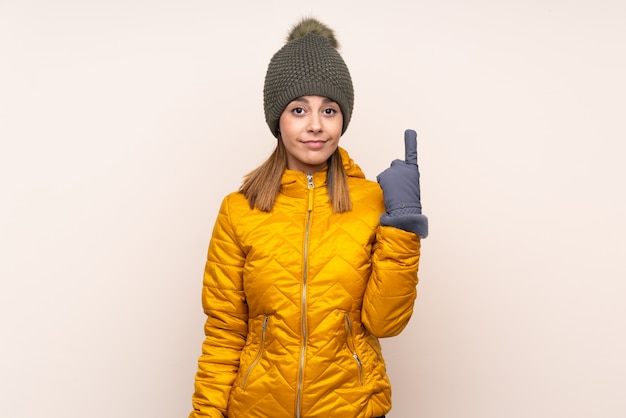 Vrouw die met de winterhoed over geïsoleerde muur met de wijsvinger een geweldig idee richt