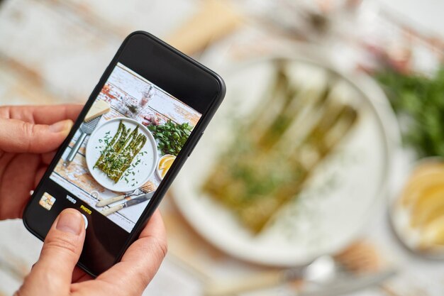 Vrouw die met een smartphone een foto maakt van vers bereid voedsel voor sociale media Gebakken aparagus met kruiden en parmesan