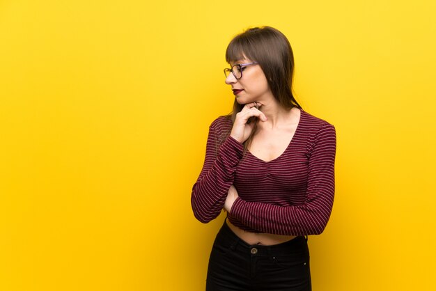 Vrouw die met glazen over gele muur aan de kant kijkt