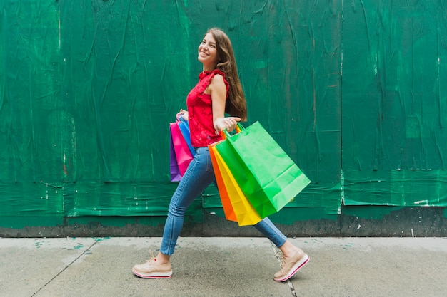 Vrouw die met het winkelen zakken op groene muurachtergrond loopt