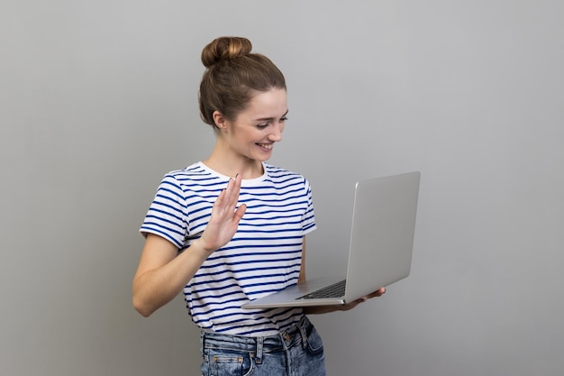 Vrouw die met laptop naar het display kijkt en met de hand zwaait en zegt hallo met videogesprek