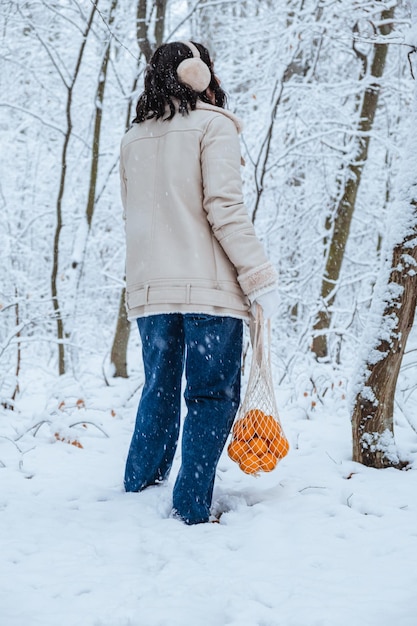 Vrouw die met mandarijnen in een rieten tas loopt op een besneeuwde dag