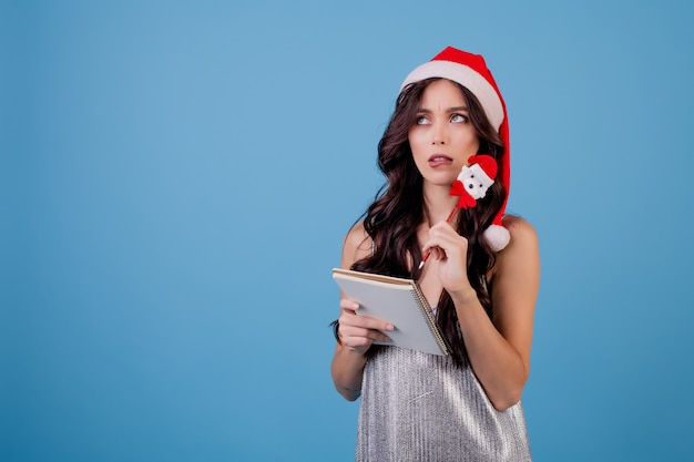 Vrouw die met notitieboekje met pen schrijft die santahoed draagt