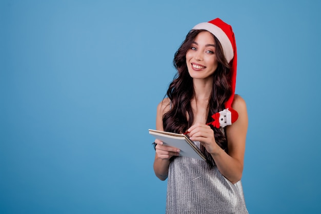 Vrouw die met notitieboekje met pen schrijft die santahoed draagt