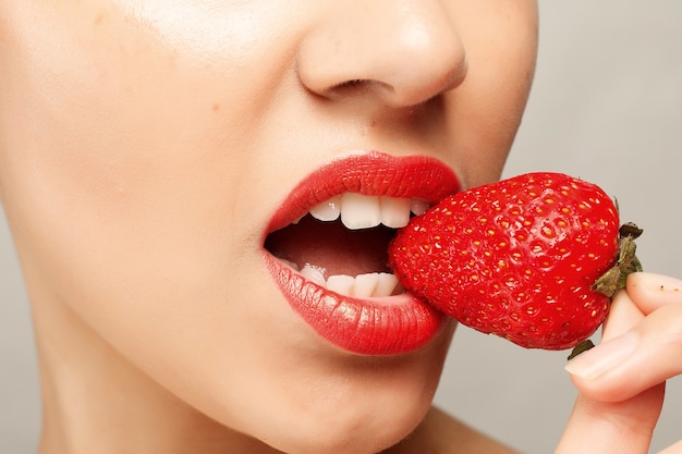 Vrouw die met rode lippen aardbei eet