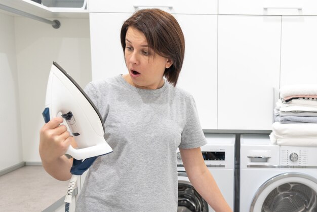 Foto vrouw die met verrassing bodem van gebroken ijzer in wasruimte bekijken met wasmachine