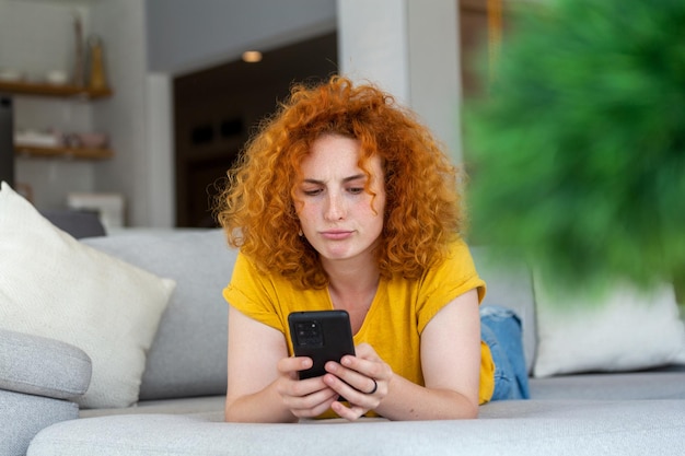 Vrouw die mobiele telefoon gebruikt terwijl ze op de bank ligt jonge vrouw rust thuis