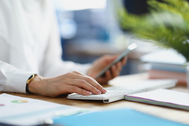 Vrouw die mobiele telefoon in handen houdt en op laptop toetsenbord typt