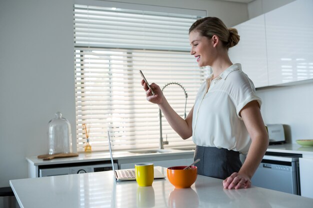 Vrouw die mobiele telefoon in keuken met behulp van