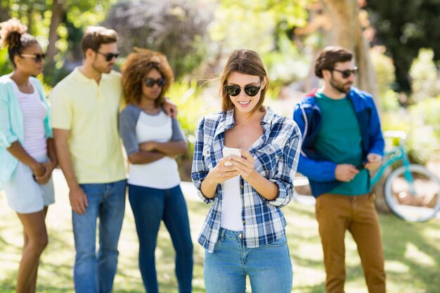 Vrouw die mobiele telefoon met vrienden op achtergrond met behulp van