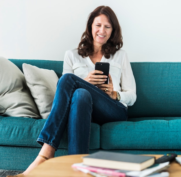 Vrouw die mobiele telefoon op de bank met behulp van