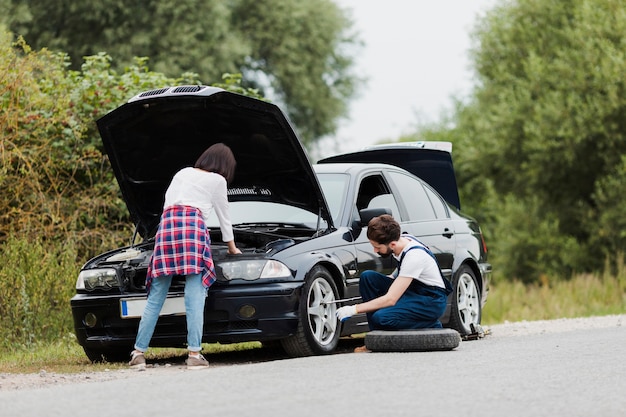 Vrouw die motor en man veranderende band controleert