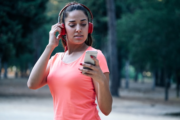 Vrouw die muziekhelmen draagt en haar mobiel in een park gebruikt