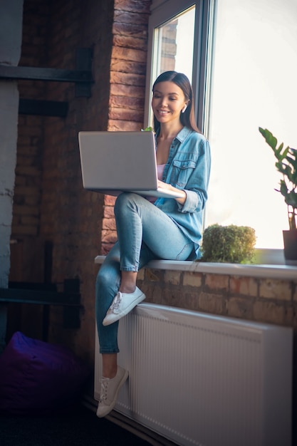 Vrouw die naar het laptopscherm kijkt terwijl ze draadloze oortelefoons draagt