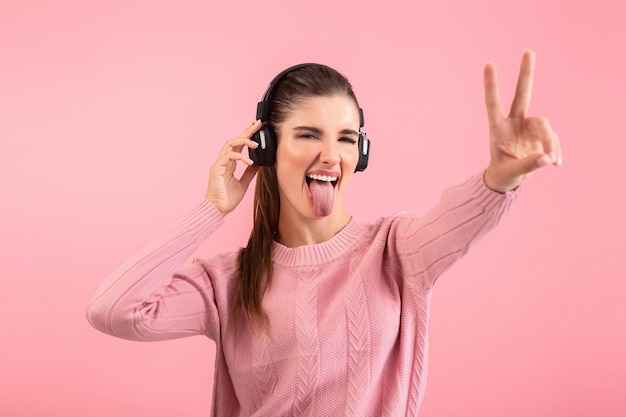 vrouw die naar muziek luistert in een draadloze koptelefoon met een roze trui die lacht, een vrolijke positieve stemming die zich voordeed op roze